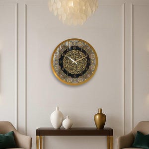 May include: A gold framed clock with Arabic calligraphy and black background. The clock is hanging on a white wall with two gold wall sconces on either side.