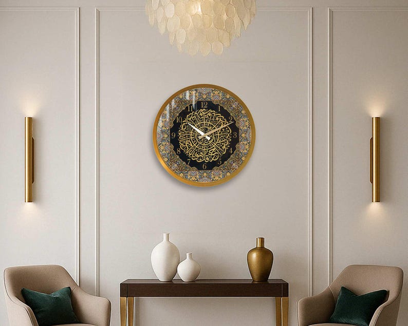 May include: A gold framed clock with Arabic calligraphy and black background. The clock is hanging on a white wall with two gold wall sconces on either side.