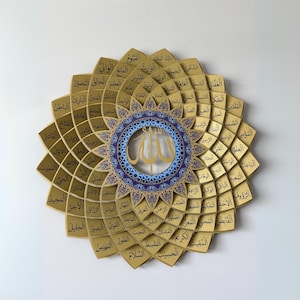 May include: A gold-colored, layered wall art piece with Arabic calligraphy. The design features a central circular element with a blue and gold pattern, surrounded by petal-shaped sections, each inscribed with text.