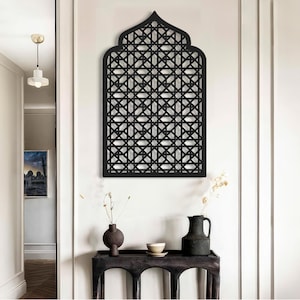 Peut inclure: Décoration murale en métal noir avec un motif géométrique complexe, ressemblant à une arche traditionnelle islamique. Le design présente un motif répétitif de carrés et de diamants, créant une pièce visuellement attrayante et élégante.