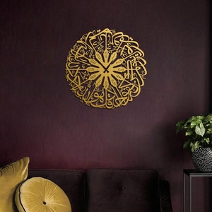 May include: A gold-colored, circular wall clock with Arabic calligraphy. The clock is mounted on a dark burgundy wall, with a sofa and decorative pillows in the foreground. A potted plant sits to the right.