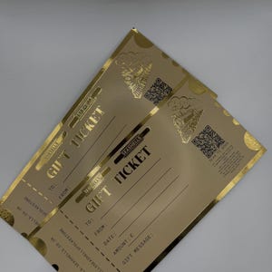 May include: Two gold gift tickets with the text "GIFT TICKET" in a bold font. The tickets have a decorative train graphic and space to fill in details like "TO:" and "FROM:." The tickets are from "SHE SELLS SEASHELLS."
