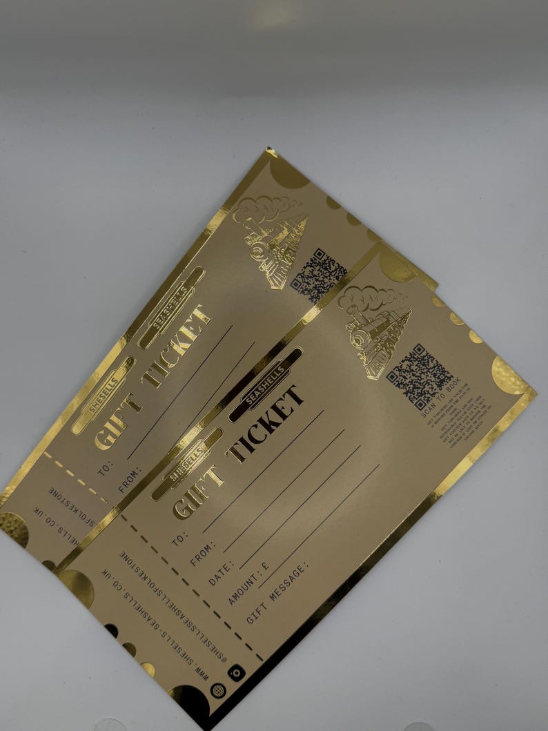 May include: Two gold gift tickets with the text "GIFT TICKET" in a bold font. The tickets have a decorative train graphic and space to fill in details like "TO:" and "FROM:." The tickets are from "SHE SELLS SEASHELLS."