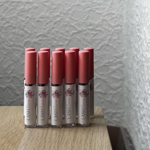 以下が含まれることがあります： ラベルに「LASH Serum」と書いてある、ピンクと透明のまつげ美容液のボトルが10本あります。
