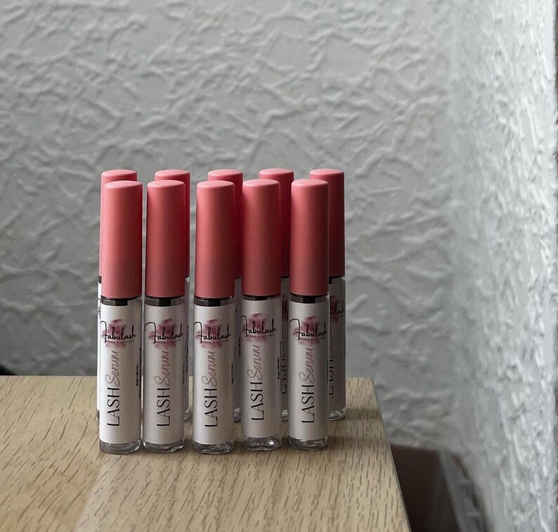 以下が含まれることがあります： ラベルに「LASH Serum」と書いてある、ピンクと透明のまつげ美容液のボトルが10本あります。