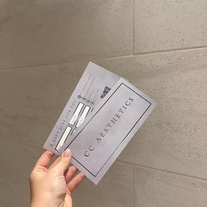 May include: A gift certificate from CC Aesthetics, held in a hand. The certificate is light gray with the text "A GIFT JUST FOR YOU" and "CC AESTHETICS". It has spaces for "TO", "VALUE", and "EXPIRY", along with a QR code.