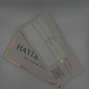 May include: Two gift certificates with gold foil accents. One certificate reads "A Gift for you" and has fields for "To", "Value", "Message", "From", and "Expiry". The other certificate reads "HAYLE THE BROW CLINIC".