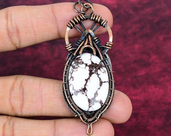 May include: A pendant featuring an oval white stone with dark brown veining, encased in a decorative frame of coiled copper wire. The wirework includes a circular top section with a small loop for hanging and intricate wrapping around the stone.