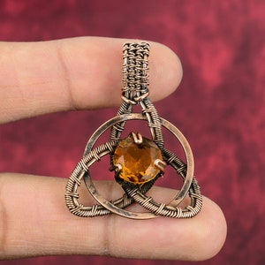 May include: A copper wire wrapped pendant with a brown gemstone in the center. The pendant is in the shape of a Celtic knot.