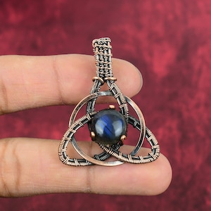May include: A copper wire wrapped pendant with a blue labradorite gemstone in the center. The pendant is in the shape of a Celtic knot.