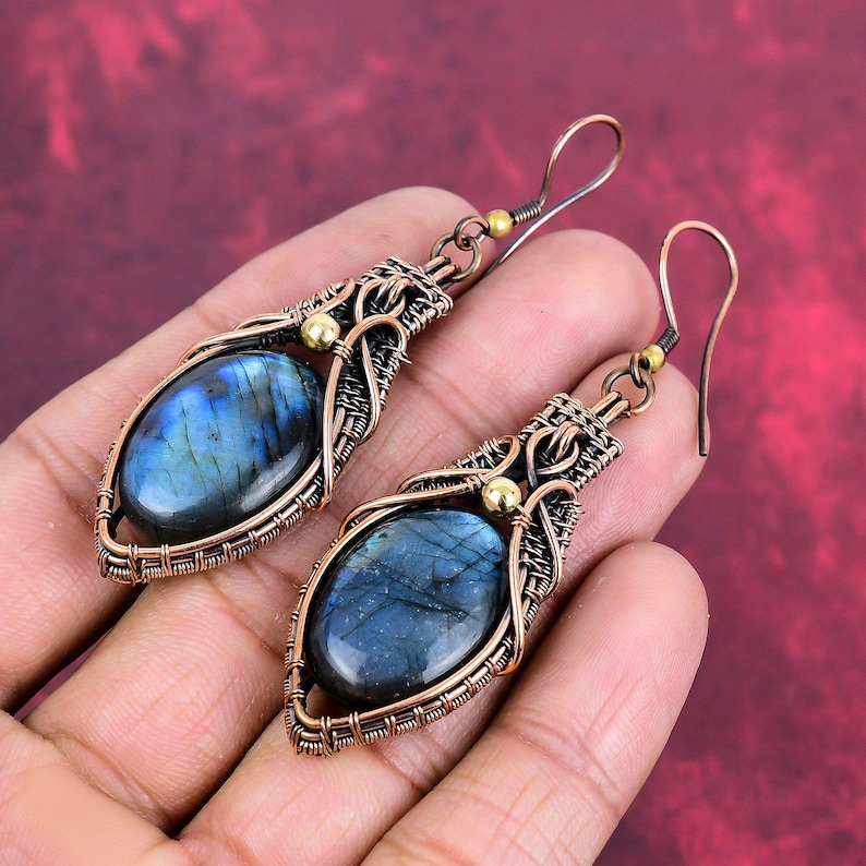 May include: A pair of copper wire wrapped earrings with oval labradorite gemstones. The earrings have a gold accent and a hook closure.