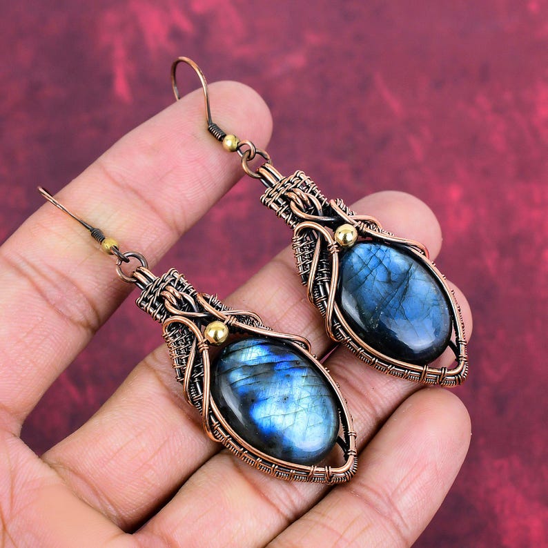 May include: A pair of copper wire wrapped earrings with oval shaped labradorite gemstones. The earrings have a gold accent on the wire wrapping.