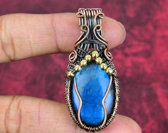 May include: A wire-wrapped pendant featuring a central oval labradorite gemstone with a blue iridescent sheen. The stone is framed by oxidized copper wire in intricate coils and loops, accented by a row of small, polished gold-tone beads.