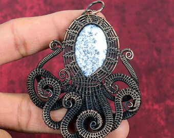 Peut inclure: Un pendentif en forme de pieuvre en fil de cuivre avec une pierre d'agate dendritique blanche et grise au centre.