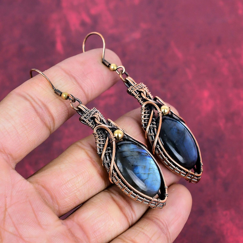 May include: A pair of dangle earrings with a blue labradorite gemstone wrapped in copper wire. The earrings have a gold accent at the top.