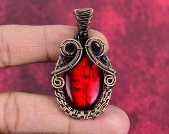May include: A red gemstone pendant with a copper wire wrap. The wire is twisted and woven into a decorative design.