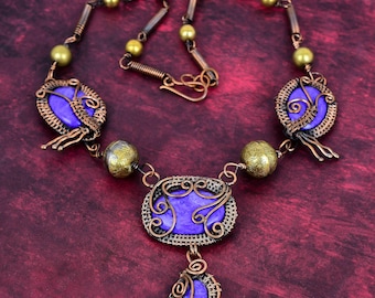 May include: A handcrafted necklace featuring purple gemstone pendants encased in copper wire. The necklace includes gold-colored beads and a copper chain. The design is intricate and ornate, with a vintage or bohemian aesthetic.