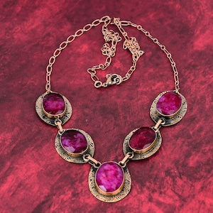 May include: A gold necklace with five oval-shaped pink stones set in ornate metal frames. The necklace has a delicate chain.