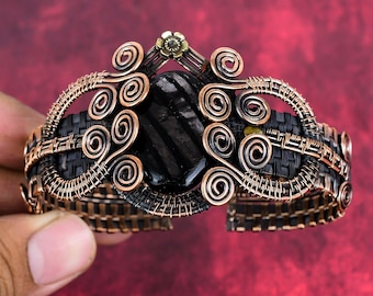 May include: A copper wire wrapped bracelet with a black gemstone and a gold flower accent.