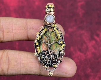 May include: A wire-wrapped pendant featuring an oval unakite stone with a copper wire tree design. The pendant is accented with small gold-toned beads and a single round white stone at the top, all secured within a detailed copper wire frame.