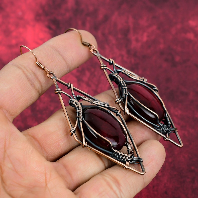 May include: A pair of copper wire earrings with a dark red gemstone in a diamond-shaped frame.