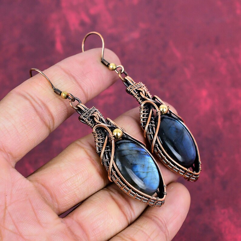 May include: A pair of dangle earrings with a blue labradorite gemstone wrapped in copper wire. The earrings have a gold accent at the top.
