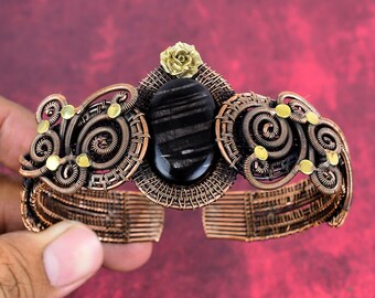 May include: A copper wire wrapped bracelet with a black gemstone and gold accents. The bracelet has a floral design and is adjustable.