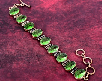 May include: A gold-toned bracelet featuring oval-shaped, bright green gemstones. The bracelet has a toggle clasp and a series of connecting links. The gemstones are set in individual gold-colored settings, creating a striking contrast.