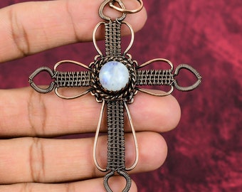 May include: A copper wire wrapped cross pendant with a round moonstone in the center. The cross is made of woven wire and has a delicate design.