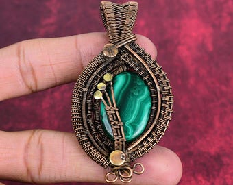 May include: A wire-wrapped pendant featuring a central oval malachite gemstone with deep green banded patterns. The setting is crafted from oxidized copper wire, incorporating intricate coils, woven textures, and small brass-toned accents.
