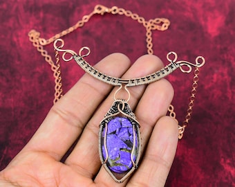 May include: A copper wire wrapped pendant necklace with a purple and black stone. The necklace has a delicate copper chain and a unique wire design.