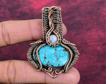 May include: A pendant featuring a large, oval-shaped turquoise stone with brown matrix veins, accented by a smaller round moonstone. The stones are encased in intricate, hand-woven copper wire work that forms a decorative frame and bail.