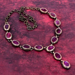 May include: A vintage-style necklace featuring oval-cut, deep red gemstones set in a bronze-toned metal. The necklace has a delicate chain and a pendant with three gemstones. The gemstones are approximately 0.5 inches in length.