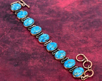 Könnte beinhalten: Ein Armband mit einer Reihe von zehn ovalen, leuchtend blauen Steinen mit dunkelbrauner Maserung, die in einen Metallrahmen gefasst sind. Das Schmuckstück verfügt über einen Knebelverschluss mit einem runden Ring und einem T-Steg am Ende.