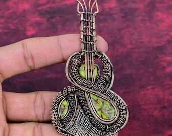 May include: A handcrafted copper wire pendant in the shape of a guitar. The pendant features green stone accents and intricate wire wrapping. The guitar-shaped pendant is a unique piece of jewelry.