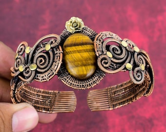 May include: A copper wire wrapped bracelet with a tiger's eye gemstone and a gold flower accent.