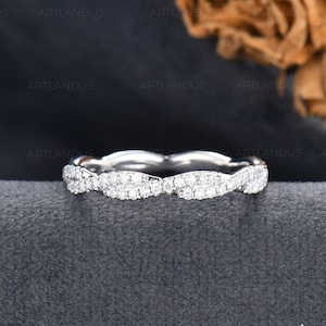 May include: A white gold ring with a continuous, intertwined design. The ring is encrusted with small, sparkling diamonds, creating a shimmering effect. The ring is set against a dark gray background, with the brand name "ARTLANDUS FINE JEWELRY" visible.
