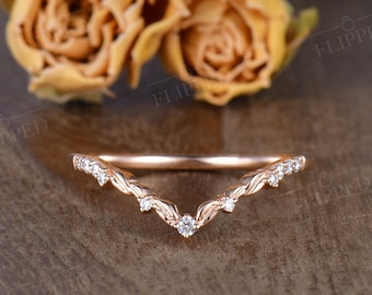 May include: A delicate rose gold wedding band with a V-shaped design and small diamonds set in the band.