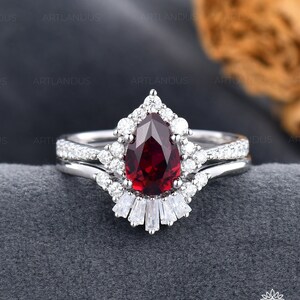 May include: A pear-shaped ruby engagement ring set with a halo of smaller diamonds and a band of baguette diamonds. The ring is set in white gold.