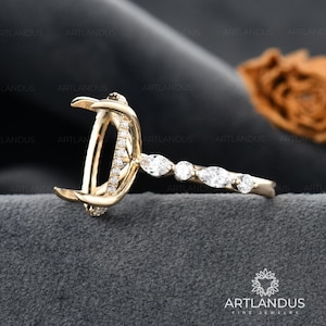 May include: A gold ring setting featuring a prominent, empty pronged basket designed to hold a large center stone. The band is adorned with a series of alternating marquise-cut and round-cut white stones, with additional small stones along the prongs.