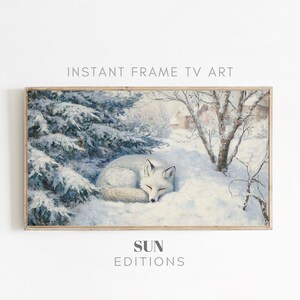 Peut inclure: Une impression encadrée d'une scène hivernale avec un renard blanc endormi dans la neige. L'œuvre d'art a une esthétique vintage, avec des arbres enneigés et un petit bâtiment en arrière-plan. Le texte "INSTANT FRAME TV ART" et "SUN EDITIONS" sont visibles.