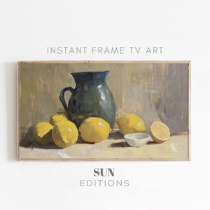 May include: A still life painting of lemons and a blue pitcher on a beige background. The painting is framed in a light wood frame. The text "INSTANT FRAME TV ART" is at the top of the image and "SUN EDITIONS" is at the bottom.