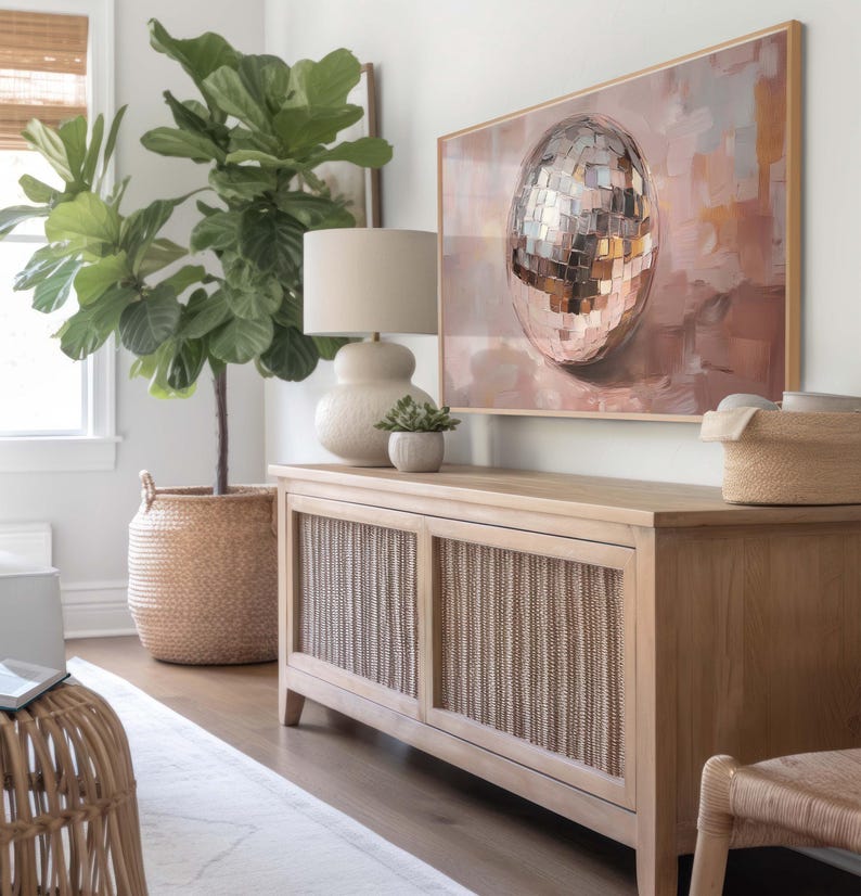 May include: A light wood cabinet with two doors featuring a woven rattan design. The cabinet is decorated with a large painting of a disco ball on a pink background. A large potted fiddle leaf fig plant is in the foreground.