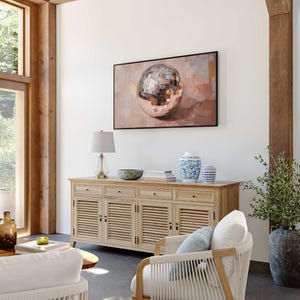 May include: A light wood cabinet with four doors and three drawers. The cabinet has a white top and is decorated with a silver disco ball painting. A white wicker chair with a blue cushion sits in front of the cabinet.