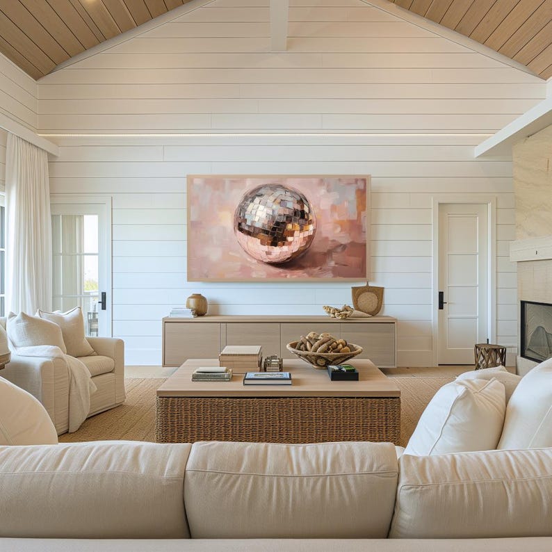 May include: A living room interior with a white couch, a coffee table, and a large painting of a silver disco ball on a pink background.