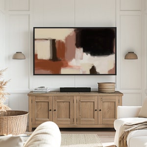 May include: A living room interior with a wooden cabinet, a white couch, and a framed abstract painting above the cabinet. The painting features shades of brown, beige, and black.