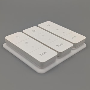 Könnte beinhalten: Drei weiße Philips Hue Smart-Lichtschalter mit einer weißen Basis. Jeder Schalter verfügt über einen Ein-/Ausschalter, eine Helligkeitssteuerung und den aufgedruckten Schriftzug "hue".