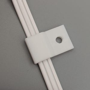 以下が含まれることがあります： ネジ用の穴が付いた白いプラスチック製のケーブルクリップ。クリップはケーブルを所定の位置に保持するように設計されています。