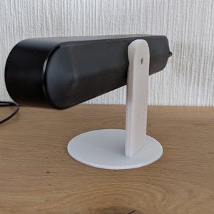 Op de afbeelding: Een zwarte speaker op een witte standaard. De standaard heeft een ronde basis en een verticale steun.