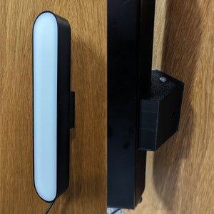 Op de afbeelding: Een zwarte rechthoekige lamp met een wit lichtpaneel gemonteerd op een houten oppervlak.